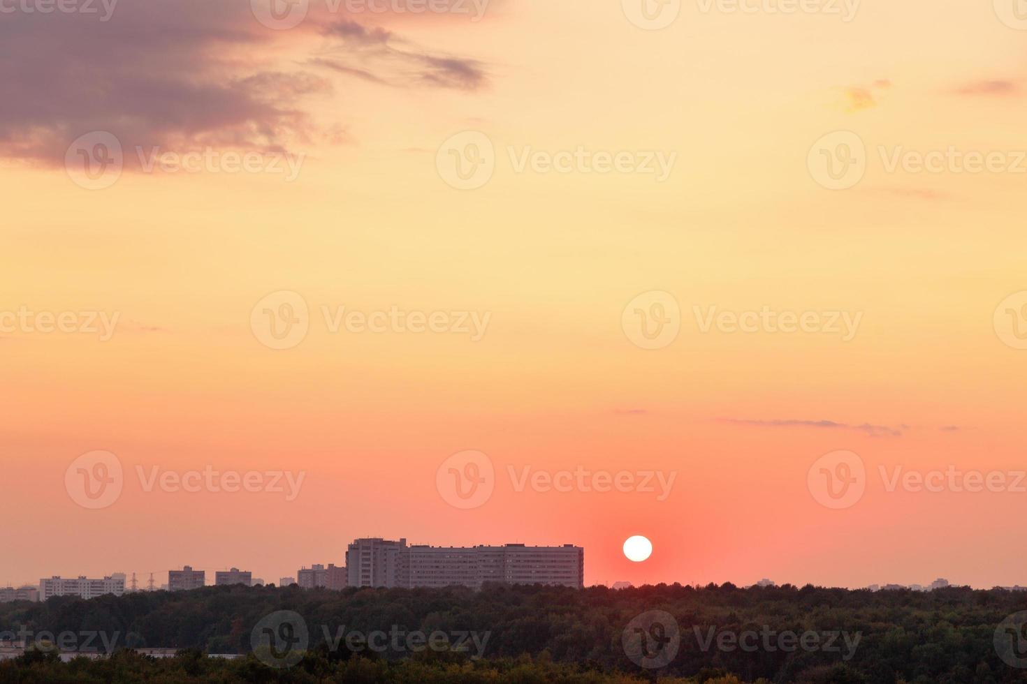 Sol ovan horisont under röd soluppgång över stad foto