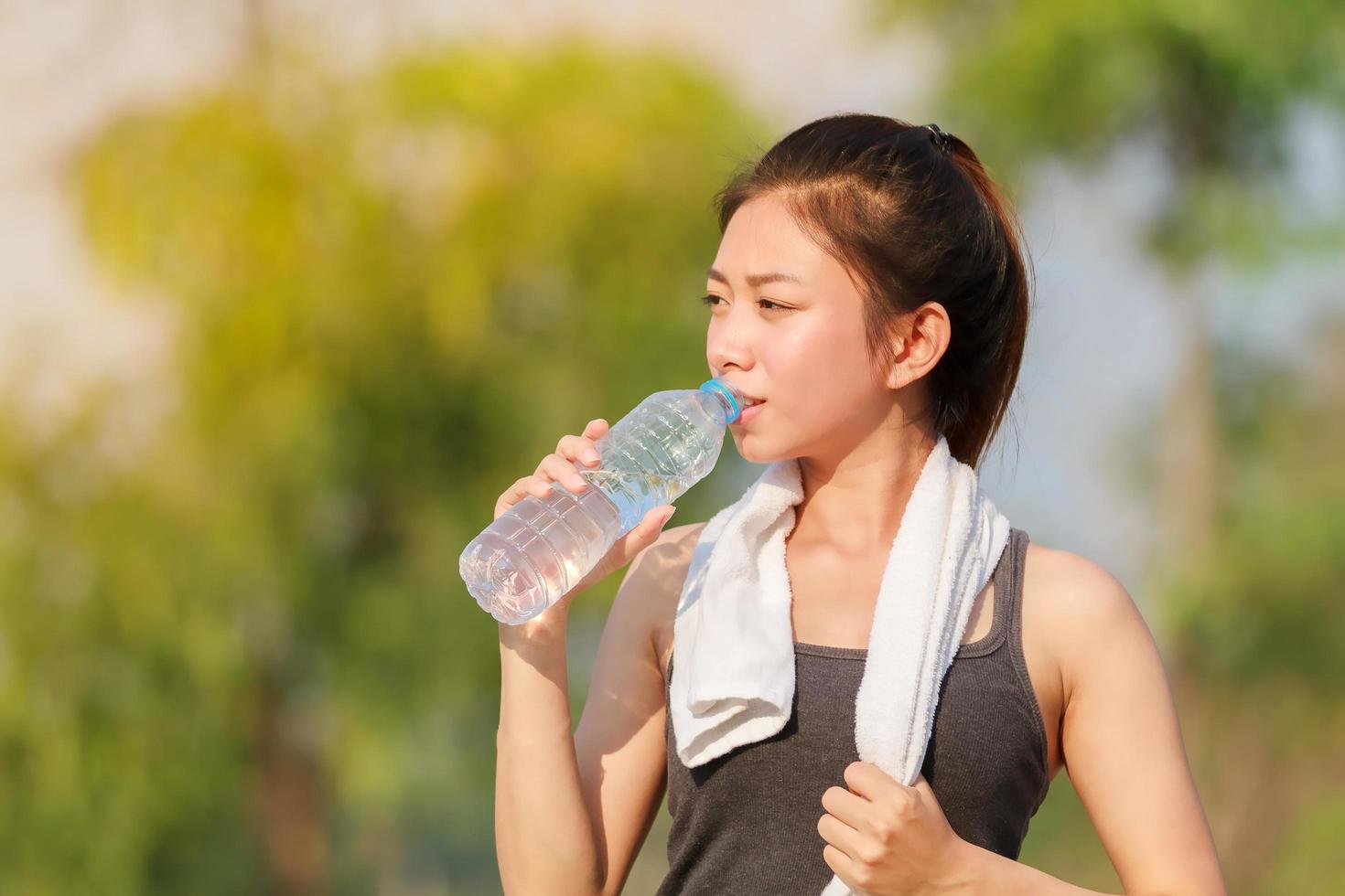 ung asiatisk kvinna som tar en vattenpaus medan hon tränar utomhus foto