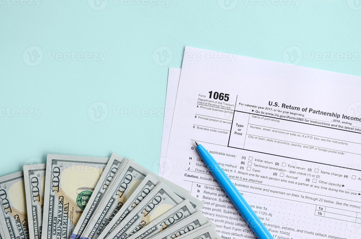 1065 beskatta form lögner nära hundra dollar räkningar och blå penna på en ljus blå bakgrund. oss lämna tillbaka för föräldraskap inkomst foto