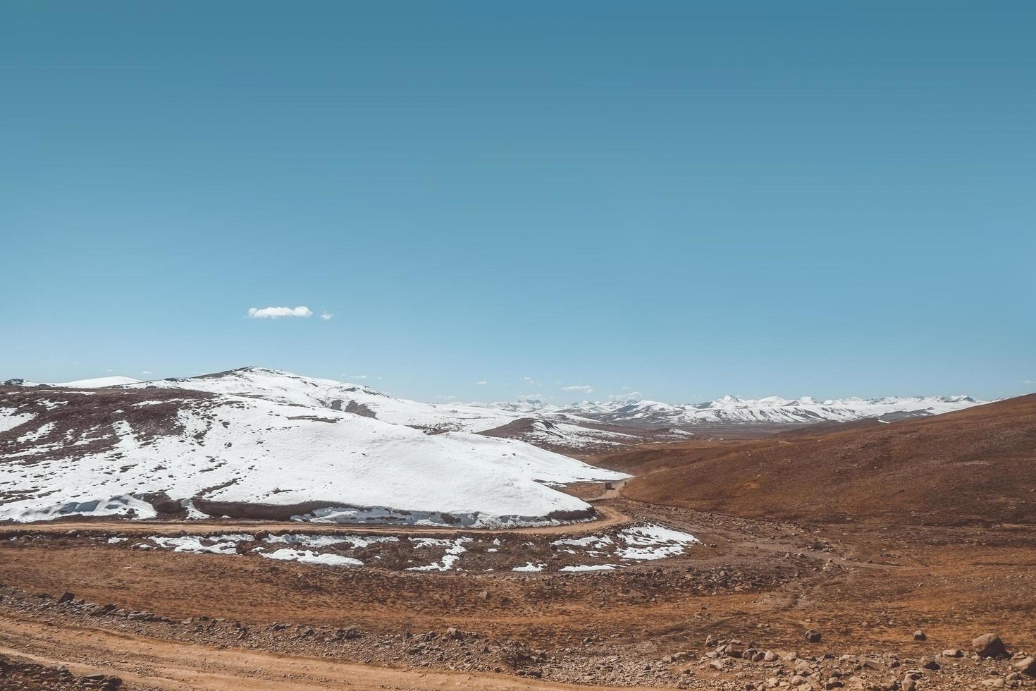 grusväg i vildmarkens bergsområde mot klar himmel foto