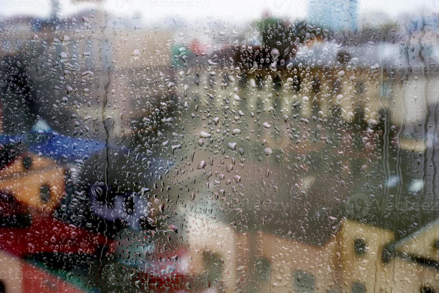 regnig fönster, regndroppar på de glas, mot de bakgrund av en stad gata med hus och en väg. mjuk suddig bakgrund. foto