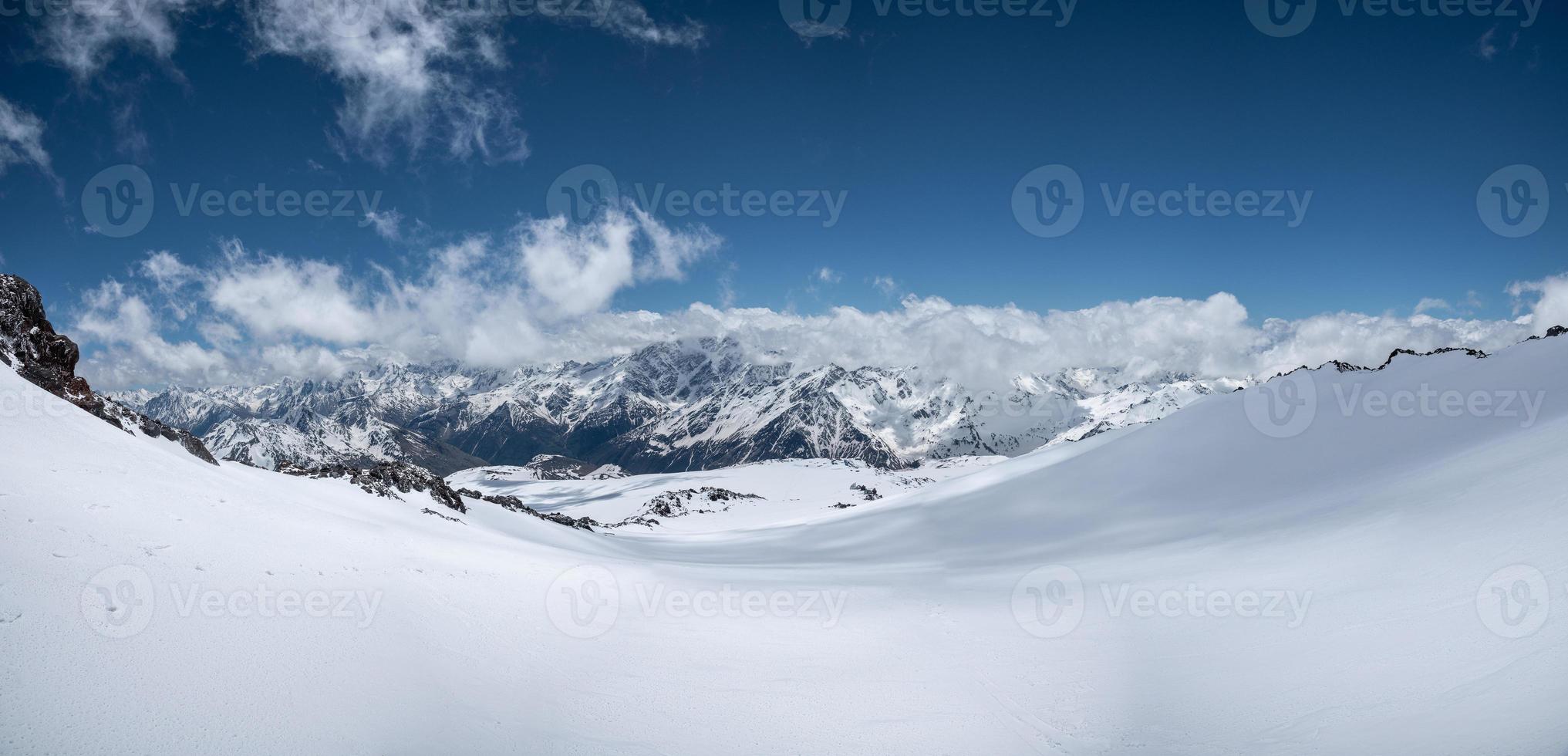 alpina panorama av de stor caucasian bergsrygg täckt med snö på en solig dag med variabel moln. idealisk sluttningar för skidor och snålskjuts åka skidor och åka snowboard foto