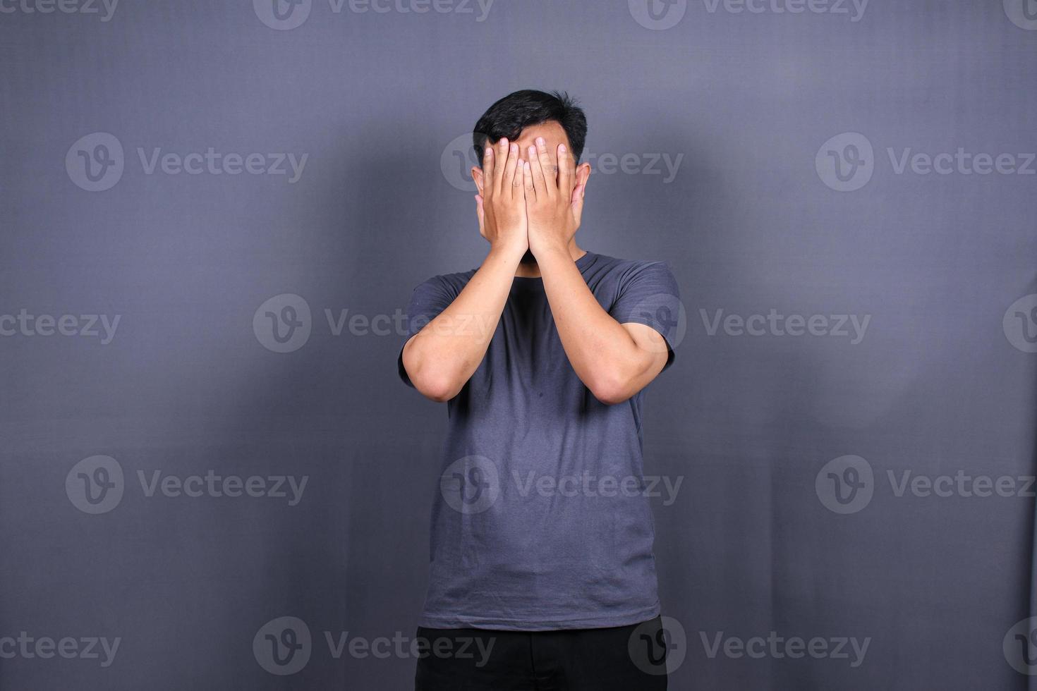 deprimerad asiatisk ung man har stressig tid med händer beläggning ansikte. isolerat på grå bakgrund. foto