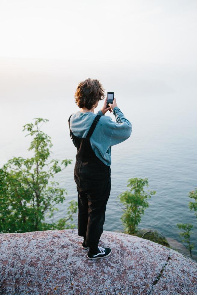 man tar foto med telefonen vid sjön