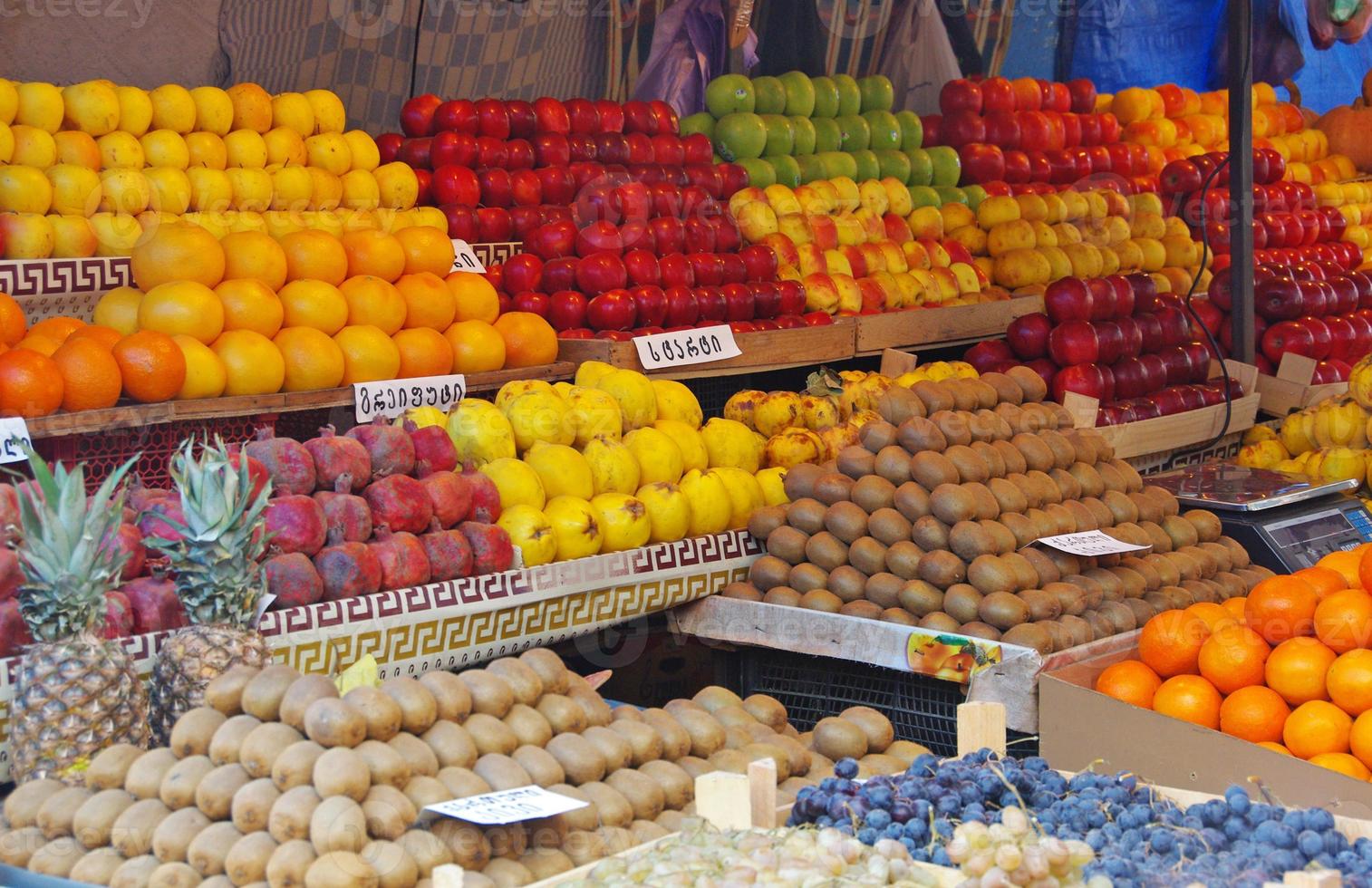 en frukt säljare bås i armenia fylld med färgrik frukt. tecken visa de namn av de respektive frukt - armeniska för apelsiner, kiwi, äpplen, kvitt foto