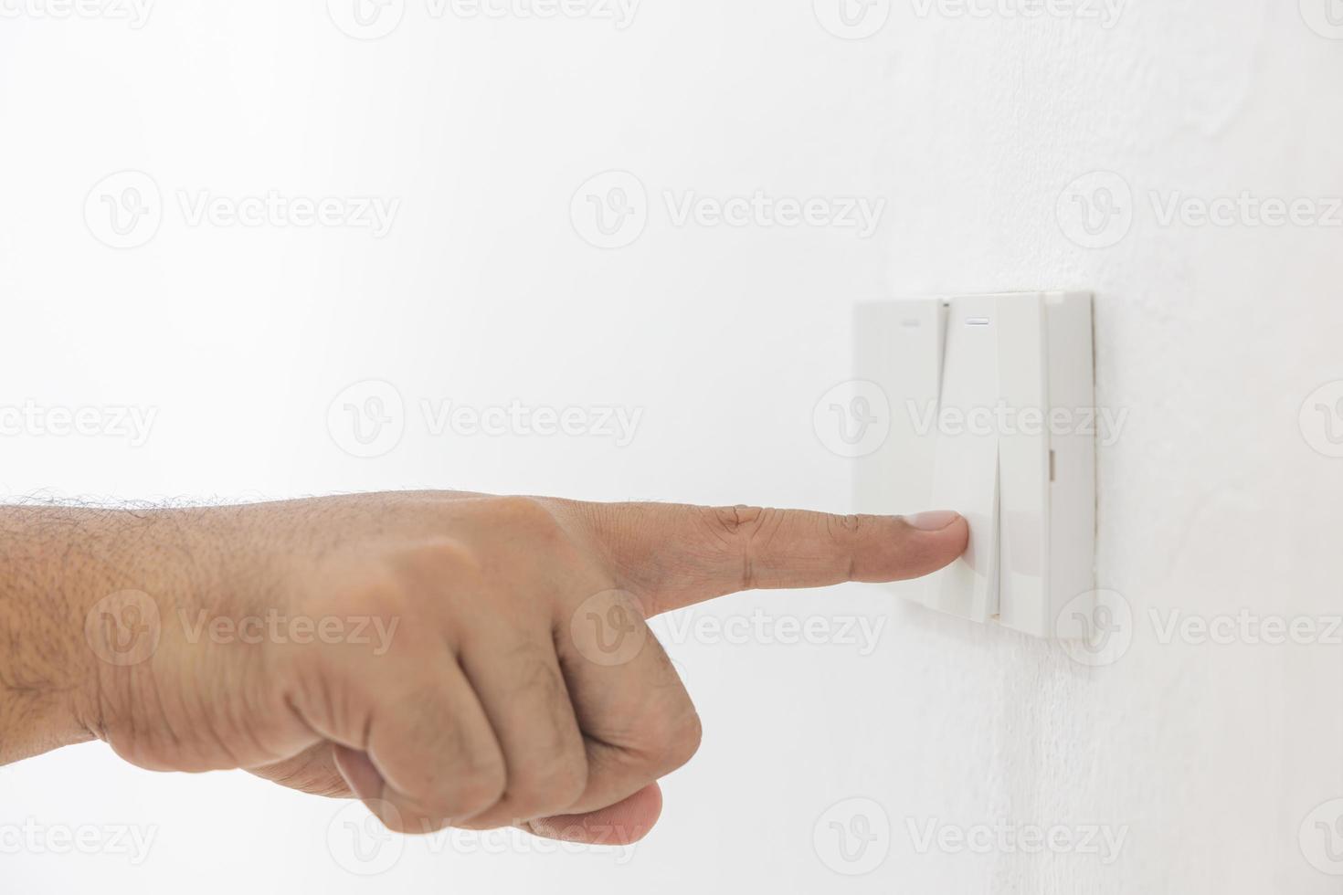 närbild ljus växla av en manlig finger kommer sväng på eller av en ljus växla med vit vägg på Hem. vit plast mekanisk växla monterad. energi, energi, spara elektricitet, kopia Plats foto