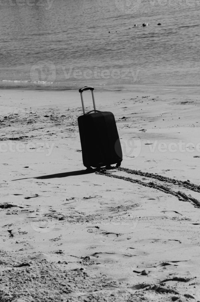 svart resa resväska på sandig strand med turkos hav bakgrund, sommar högtider begrepp foto