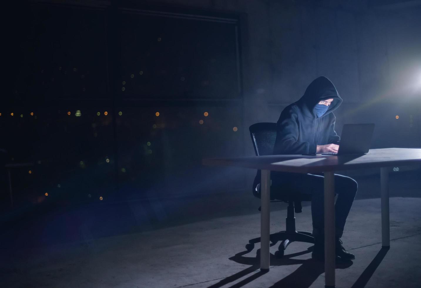 hacker använder sig av bärbar dator dator medan arbetssätt i mörk kontor foto