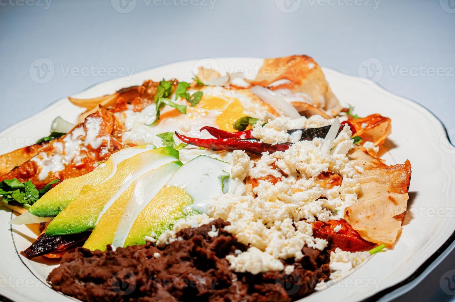 chilaquiles mexikansk mat med i röd sås, ost, grädde och chili paprikor på årgång bakgrund foto
