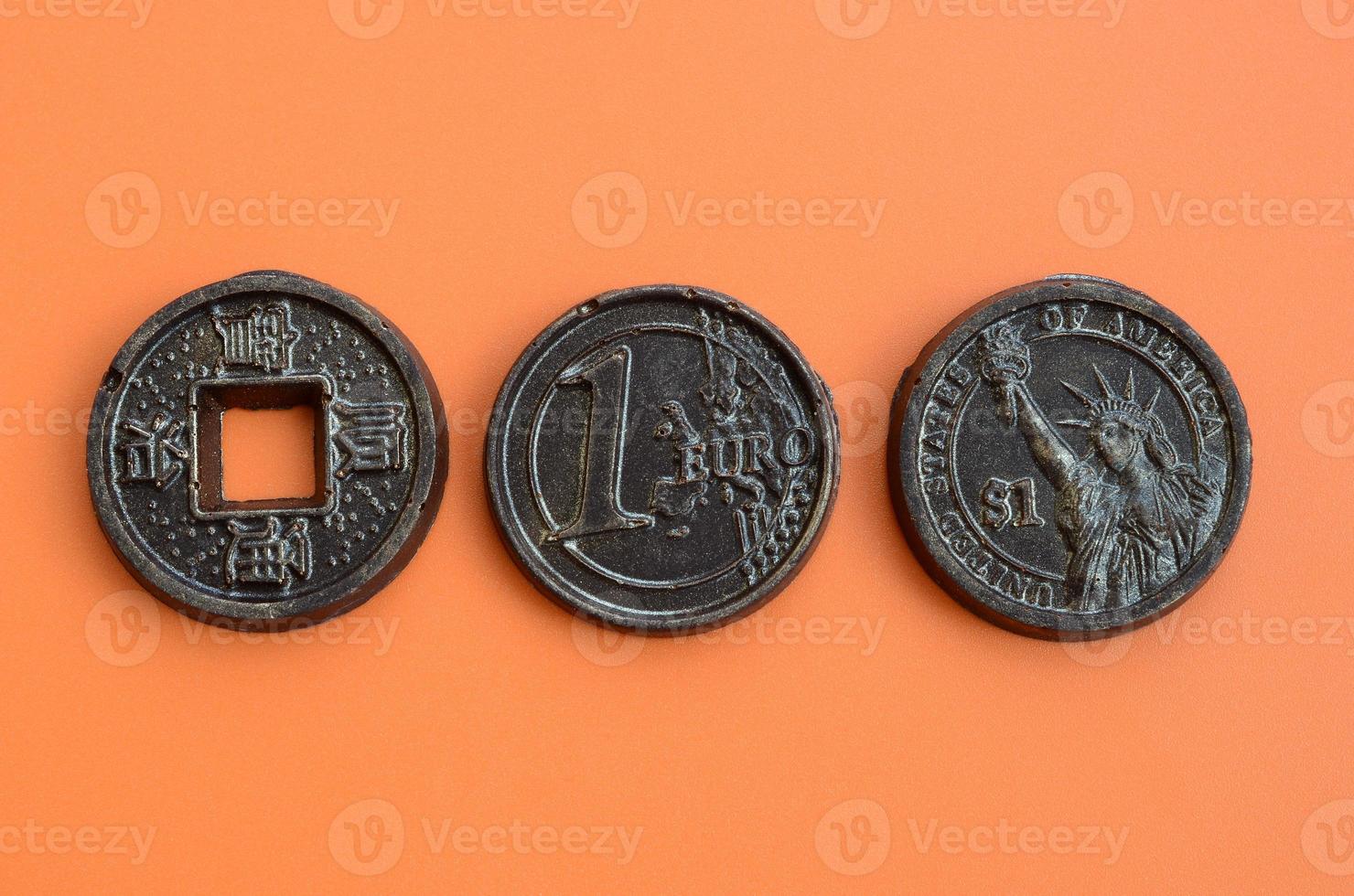 tre choklad Produkter i de form av euro, USA och japan mynt lögn på ett orange plast bakgrund. en modell av kontanter mynt i ett ätlig form foto