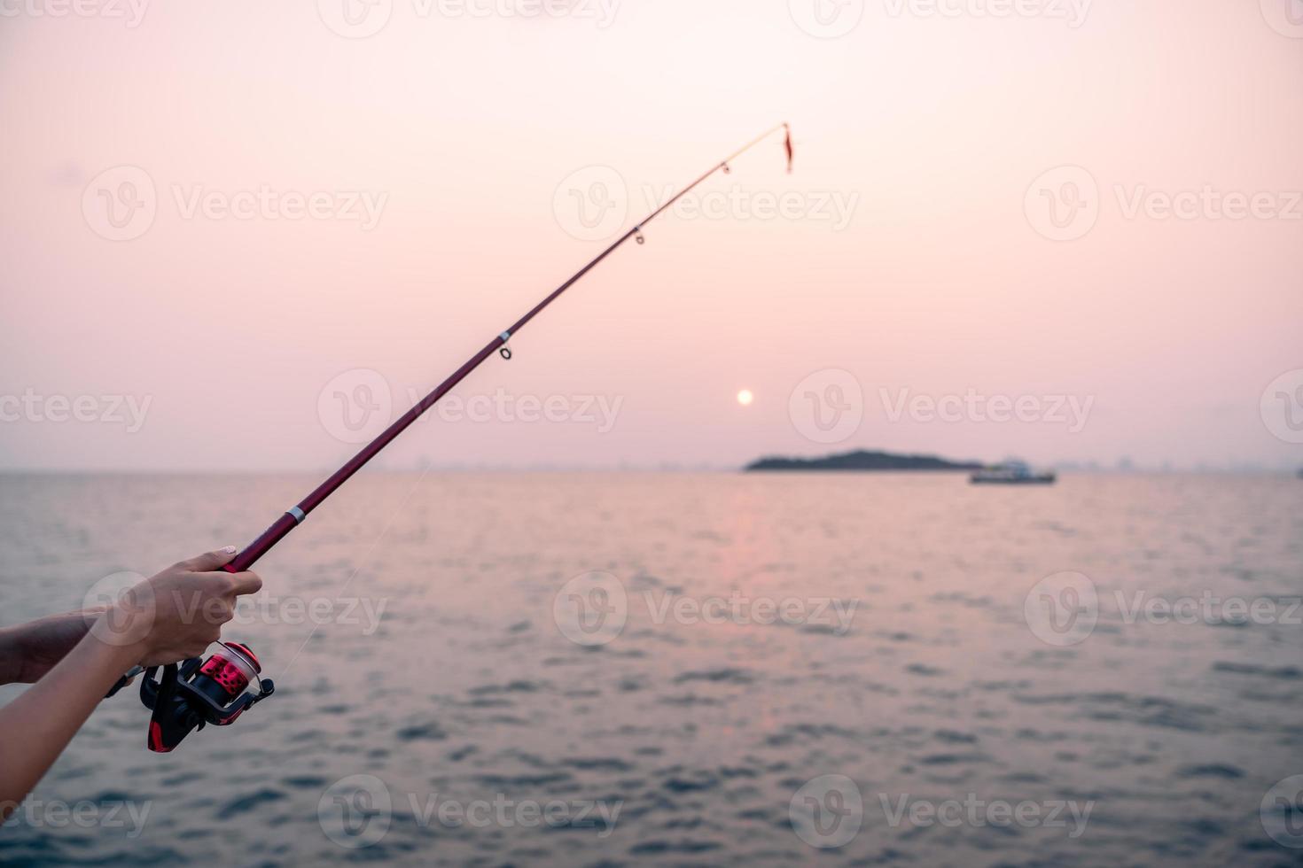 kvinna hand innehav fiske stång med hav bakgrund, fiske på solnedgång. foto