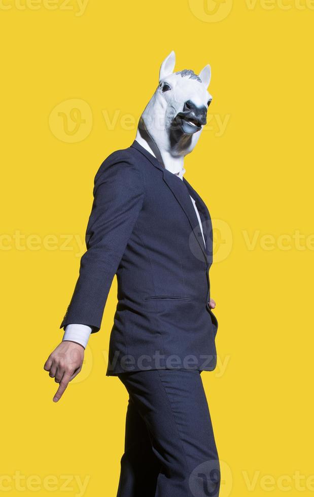 en vertikal skott av en kreativ man i en kostym med en vit häst mask Framställ på en gul bakgrund vägg. foto