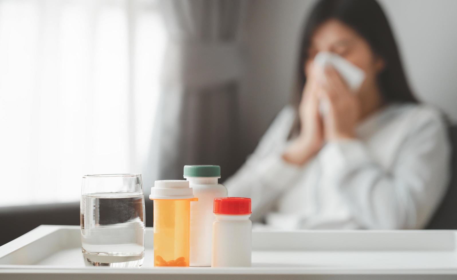 mediciner och ett glas vatten med en sjuk kvinna i bakgrunden foto