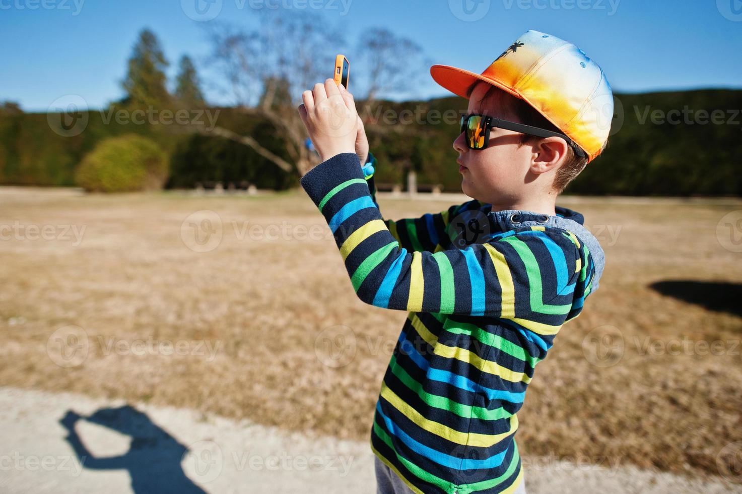 pojke i mössa och solglasögon gör foto via telefon i lednice park, Tjeckien.