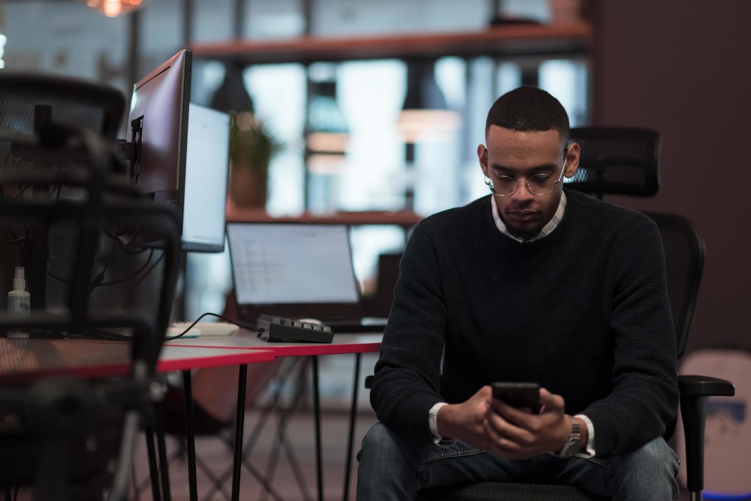 ung afrikansk amerikan arbete i coworking Plats använder sig av smartphone analyserar uppkopplad marknadsföra trender, fokuserade man arbetstagare läsning finansiell Nyheter eller bläddring internet på telefon. teknologi begrepp foto