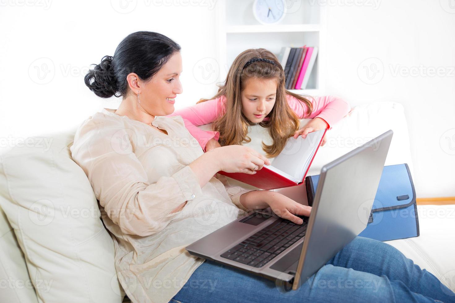 mamma och dotter som sitter på soffan och använder bärbar dator foto