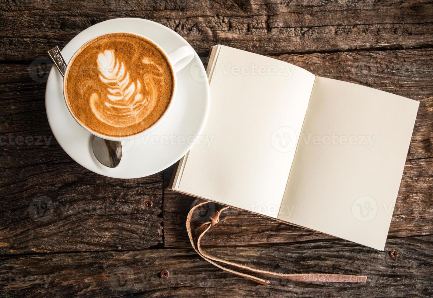 en kopp av varm kaffe med latte konst på de yta med de läder bok på de trä- tabell. foto