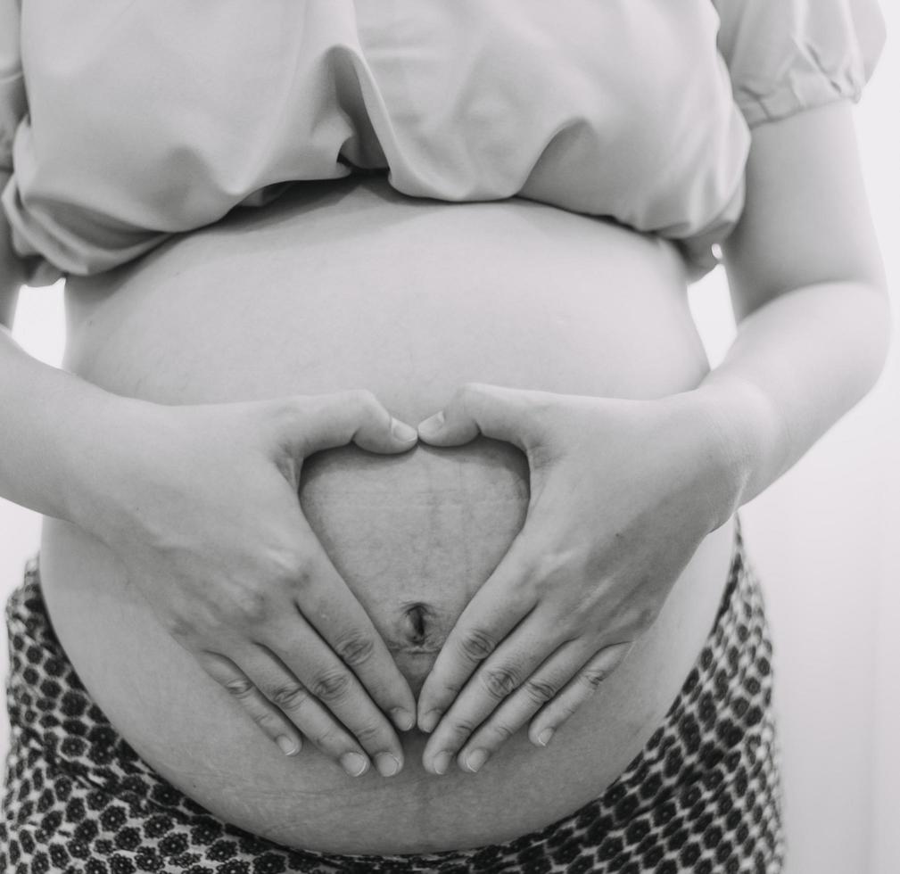 ung vuxen gravid kvinna i vit kläder rörande stor naken mage med händer. som visar form. graviditet begrepp. förväntan tid. närbild. isolerat på ljus grå vägg bakgrund. foto