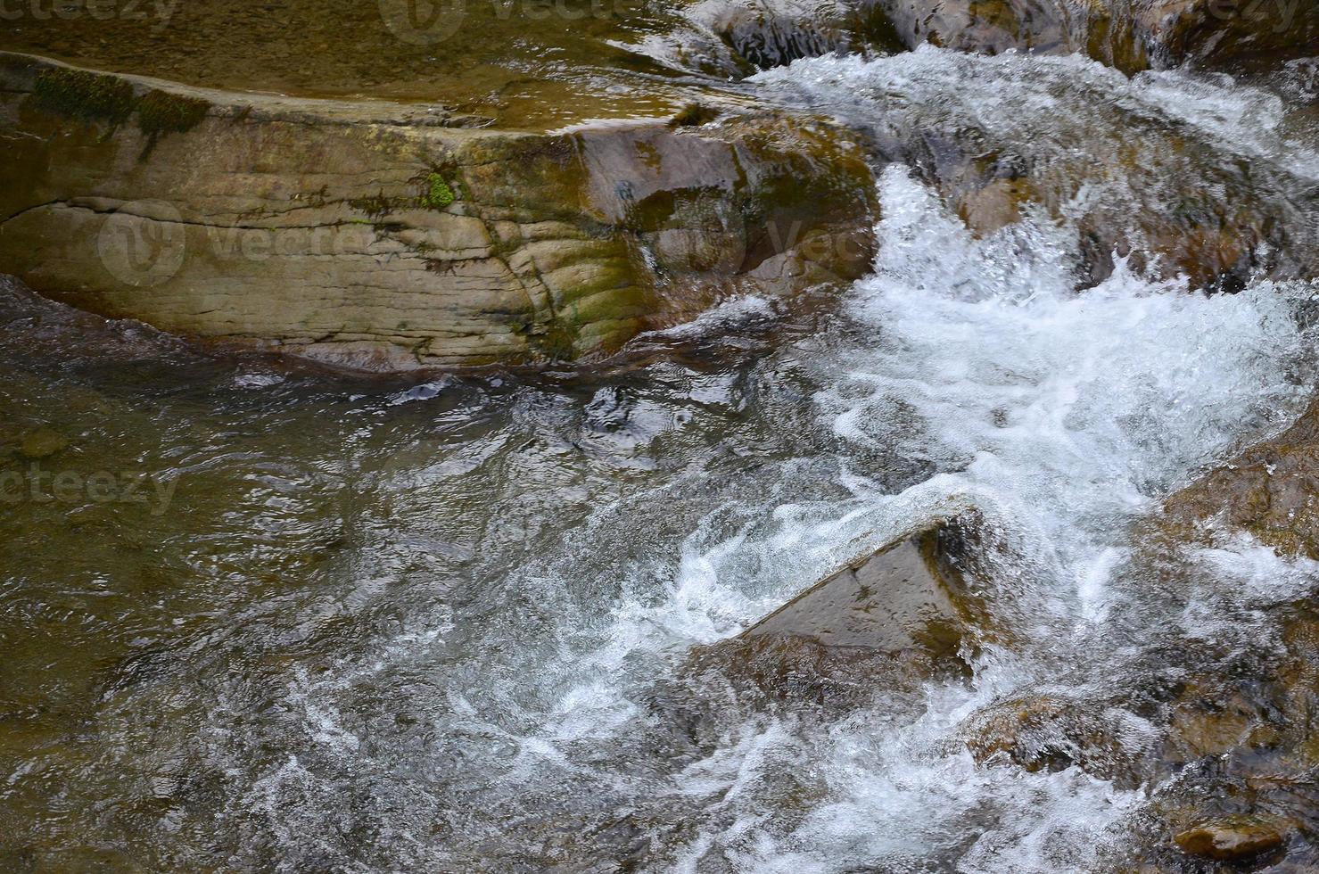 närbild bild av en små vild vattenfall i de form av kort strömmar av vatten mellan berg stenar foto