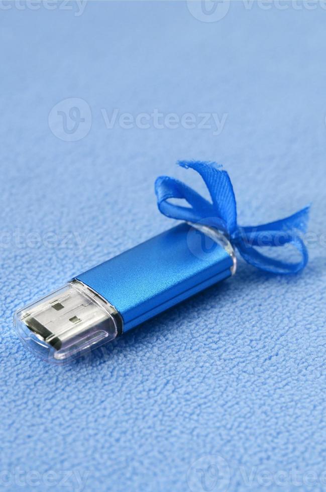 lysande blå uSB blixt minne kort med en blå rosett lögner på en filt av mjuk och hårig ljus blå skinna tyg. klassisk kvinna gåva design för en minne kort foto