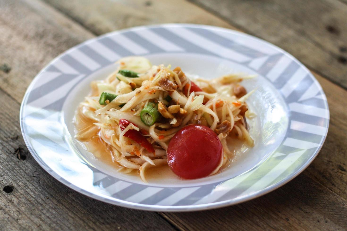 thai papaya sallad på en tallrik, papaya sallad med bajs, citron, peppar, röd tomat i vit skål på trä- tabell foto