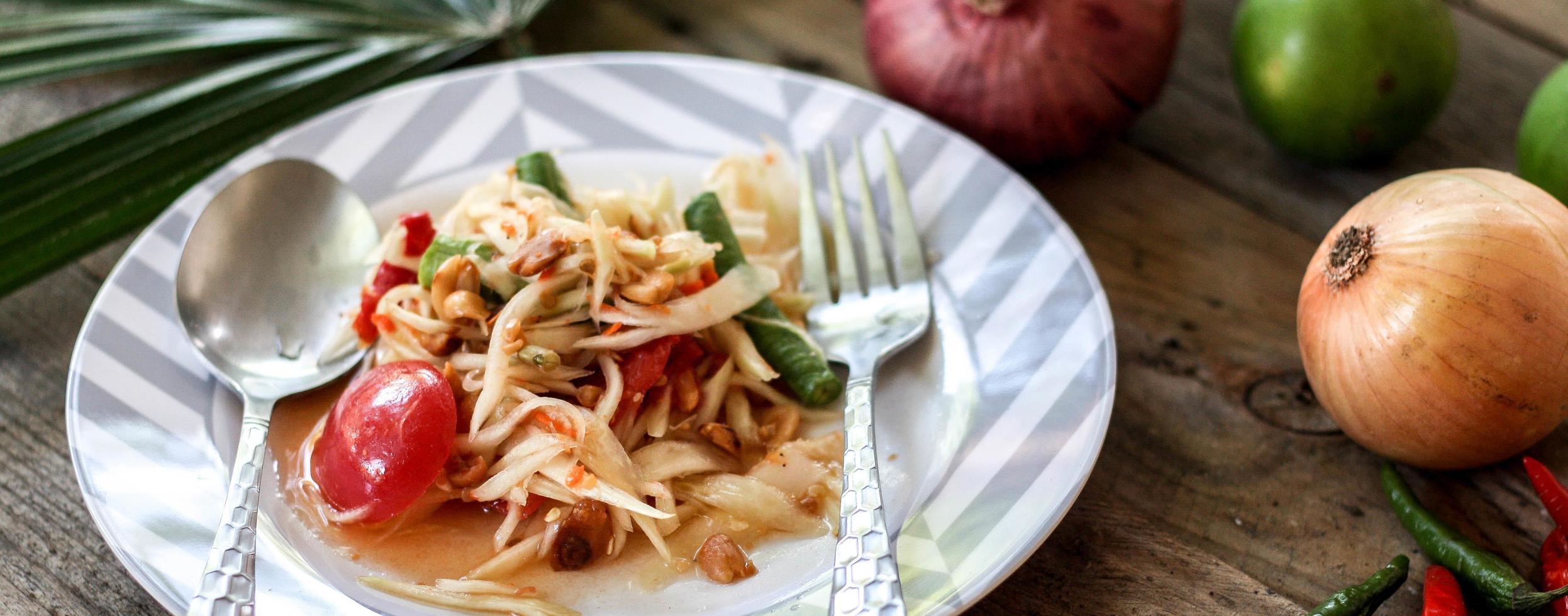 thai papaya sallad på en tallrik, papaya sallad med bajs, citron, peppar, röd tomat i vit skål på trä- tabell foto