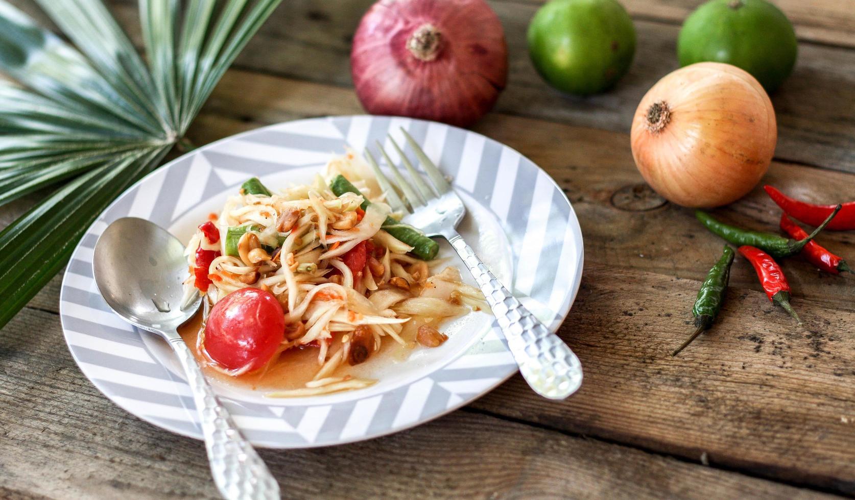 thai papaya sallad på en tallrik, papaya sallad med bajs, citron, peppar, röd tomat i vit skål på trä- tabell foto