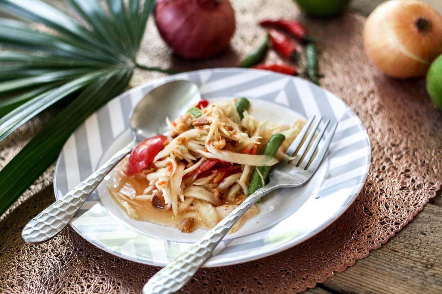 thai papaya sallad på en tallrik, papaya sallad med bajs, citron, peppar, röd tomat i vit skål på trä- tabell foto