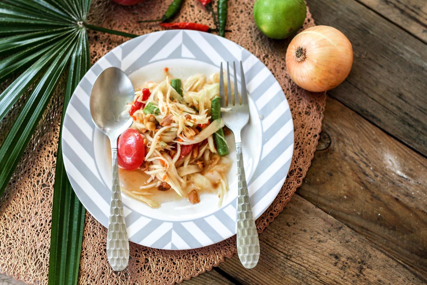 thai papaya sallad på en tallrik, papaya sallad med bajs, citron, peppar, röd tomat i vit skål på trä- tabell foto