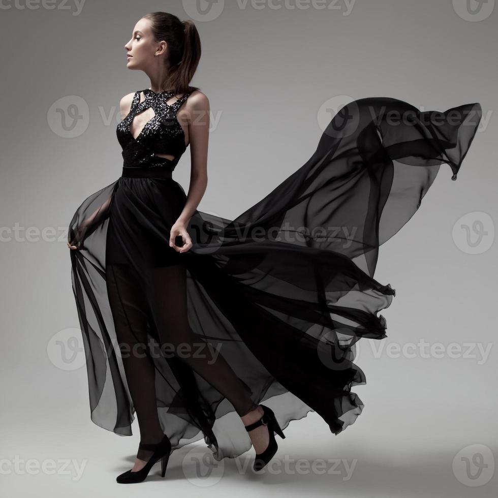 modekvinna i fladdrande svart klänning. grå bakgrund. foto