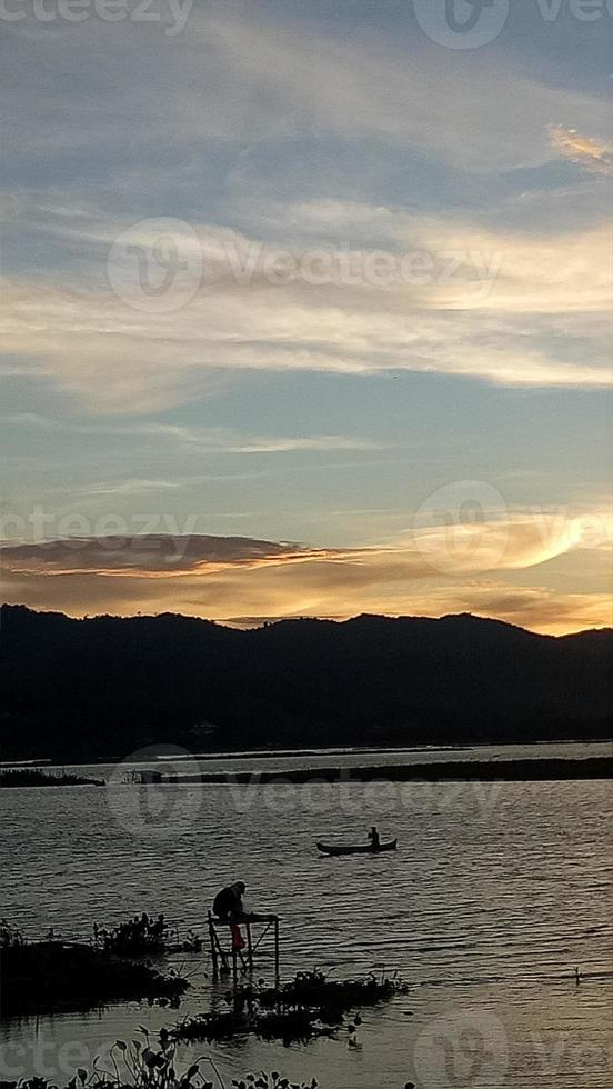 silhuett av en man fiske i de eftermiddag. solnedgång på sjö limboto, indonesien foto
