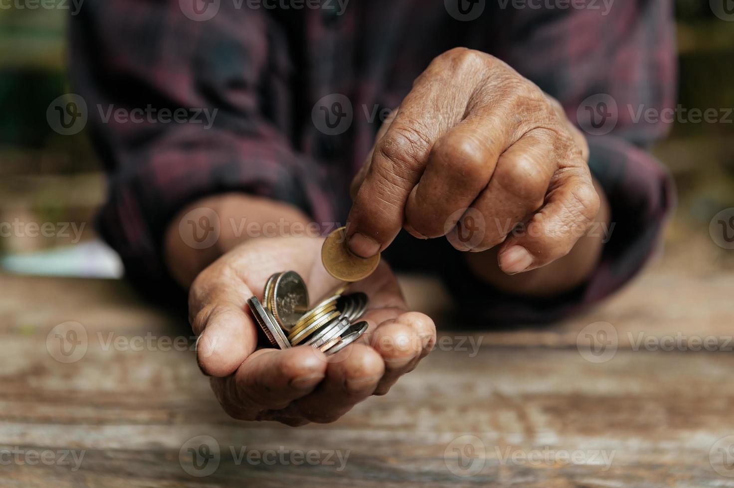 hand gammal man tiggeri för pengar eftersom av de hunger på de trä tabell. foto