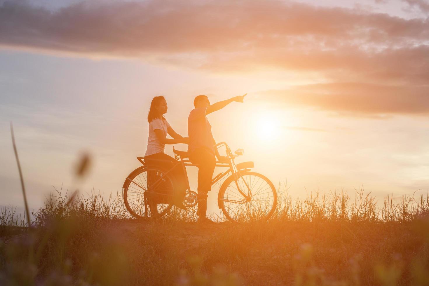 silhuett av ljuv ung par i kärlek Lycklig tid på cykel foto