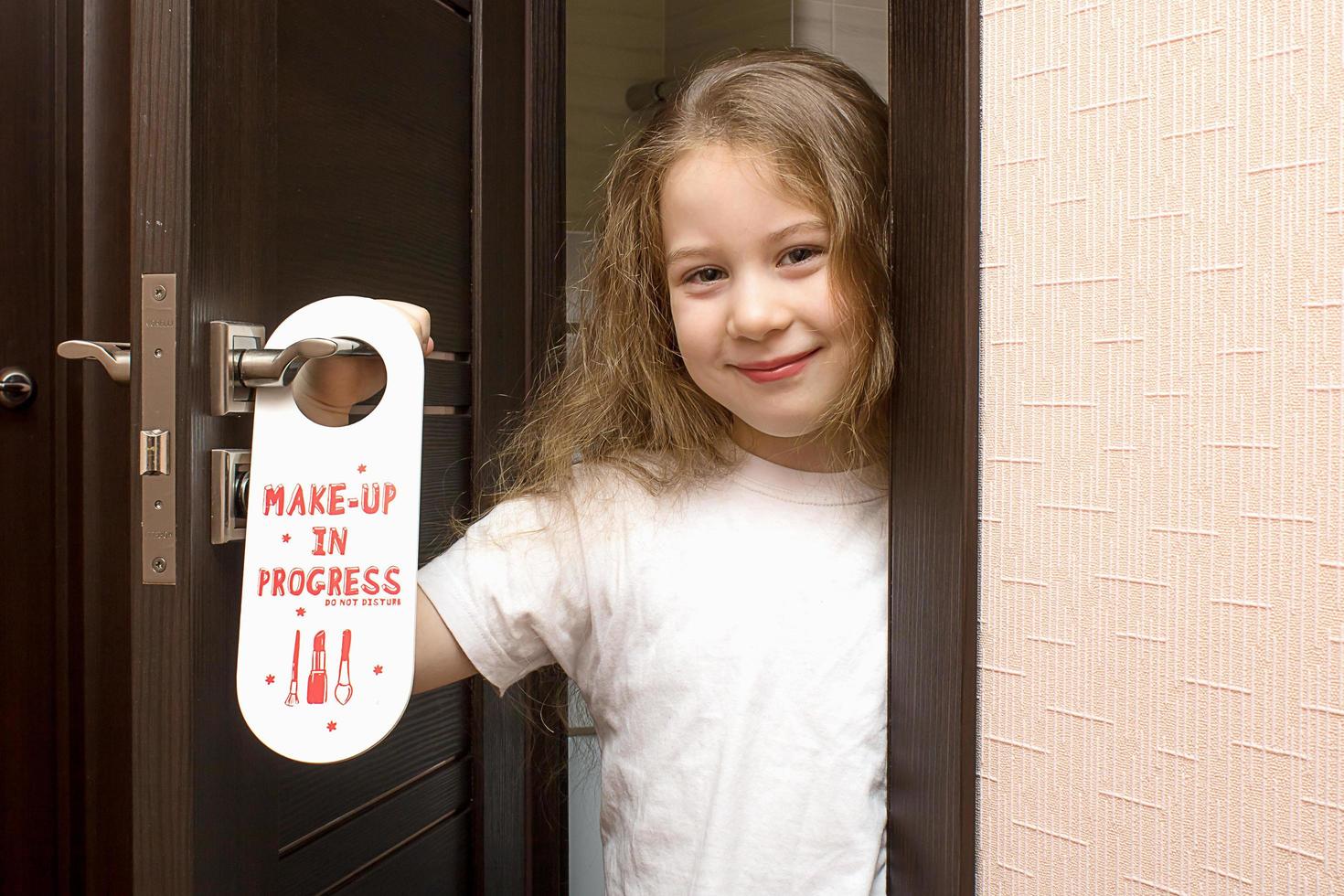 en liten flicka med målad mun kikar ut från Bakom en dörr den där säger do inte störa smink i framsteg foto