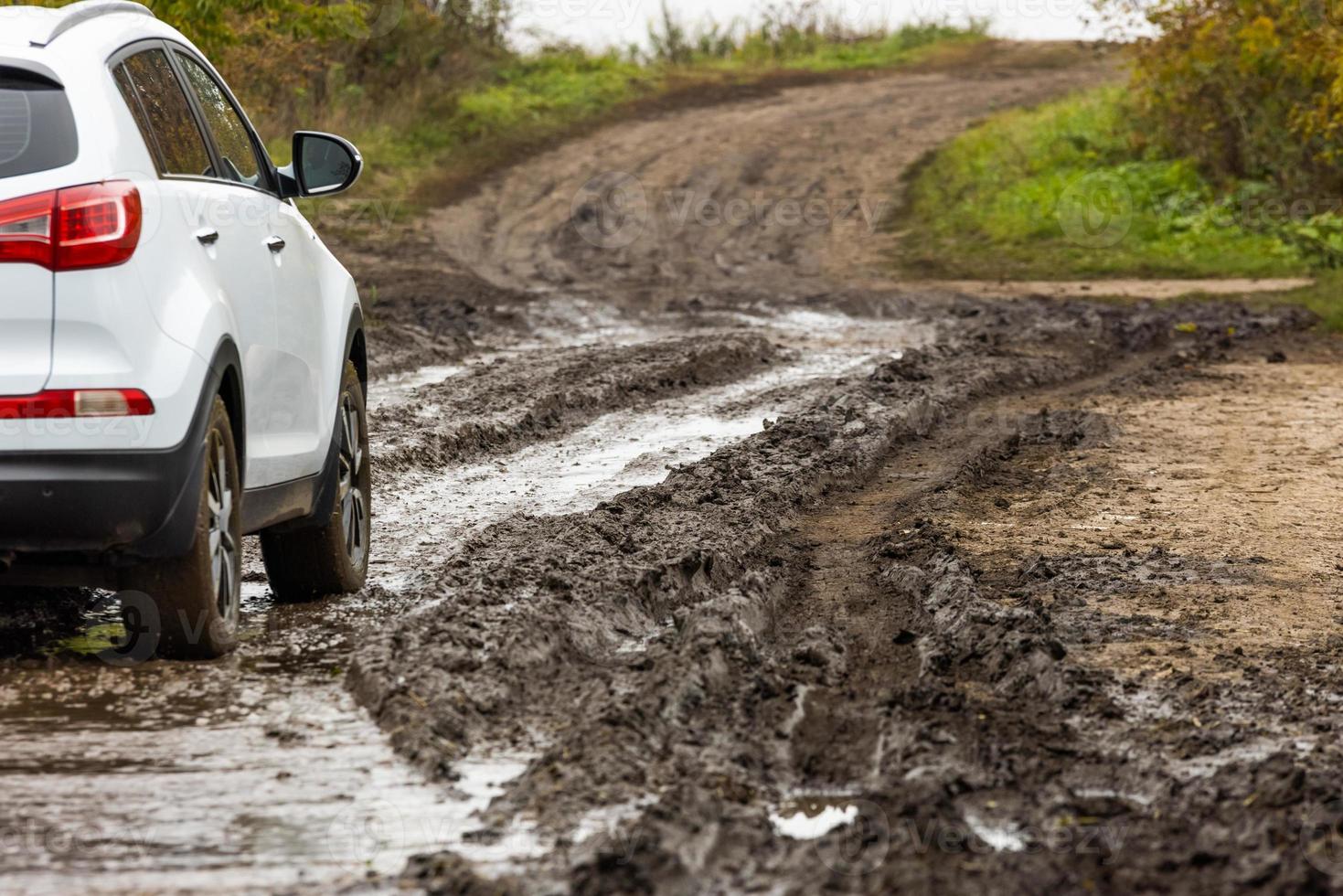 rena vit sUV bil rör på sig på smuts väg med våt lera i främre av suddigt backe foto
