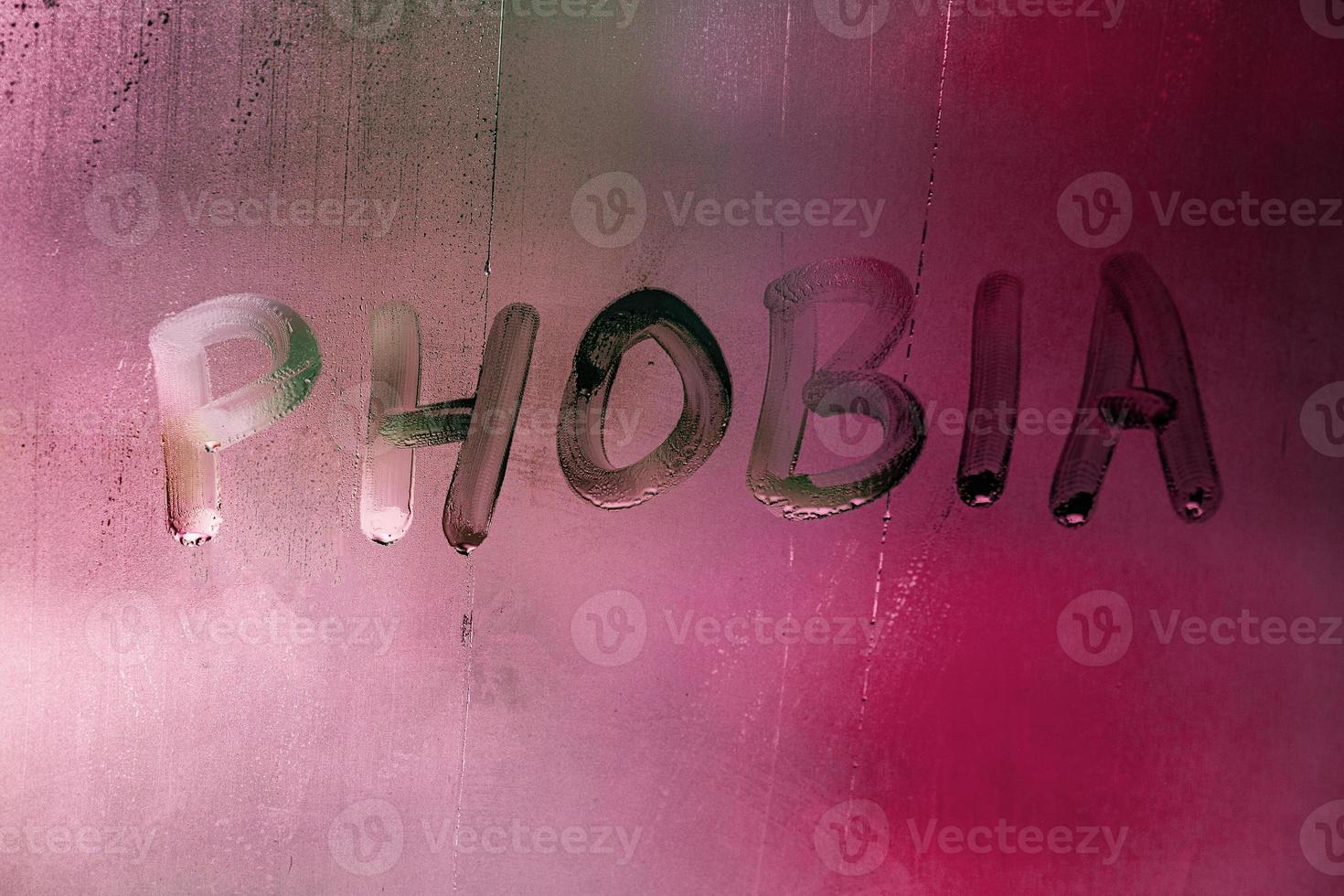 de ord fobi handskriven på våt dimmig fönster glas yta med röd bakgrund ljus foto