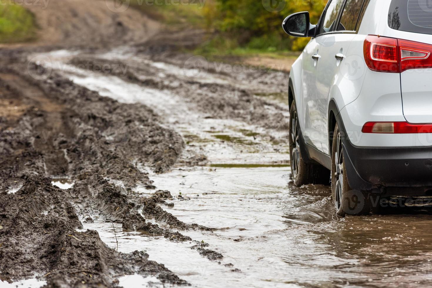 rena vit sUV bil rör på sig längs smuts väg med våt lera i främre av suddigt backe foto