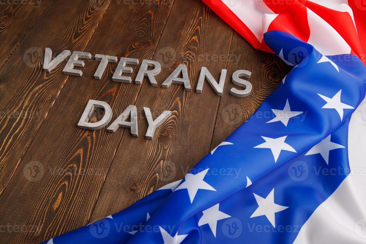de ord veteraner dag lagd med silver- metall brev på trä- styrelse yta med skrynkliga USA flagga på rätt sida med diagonal perspektiv foto