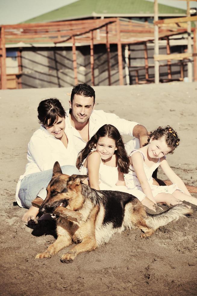 Lycklig familj spelar med hund på strand foto