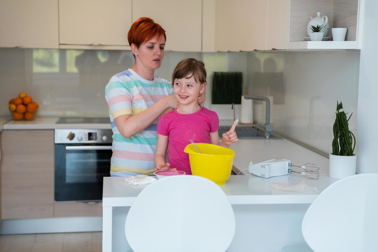 rolig liten flicka hjälpare spelar med deg på hans händer inlärning till knåda hjälper vuxen mamma i de kök, Lycklig söt bebis dotter och förälder mamma ha roligt matlagning småkakor. foto