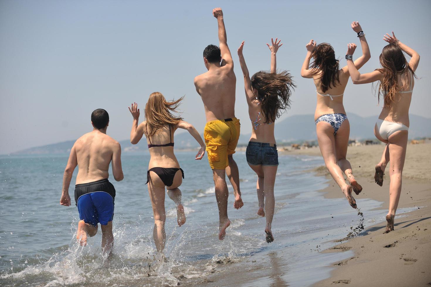 Lycklig människor grupp ha roligt och löpning på strand foto