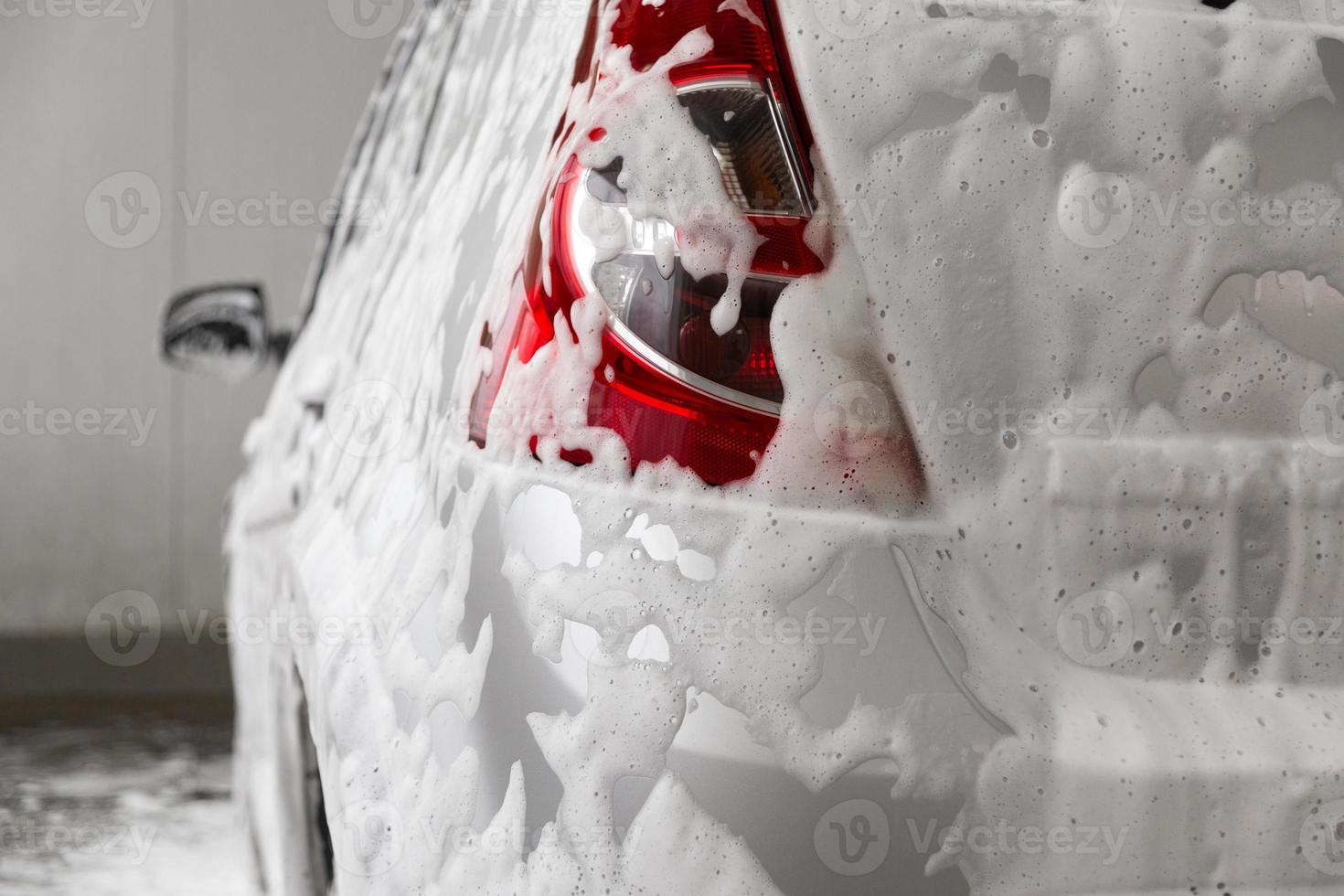en bil täckt förbi tvål skum medan tvättning inomhus - närbild se från tillbaka med selektiv fokus foto