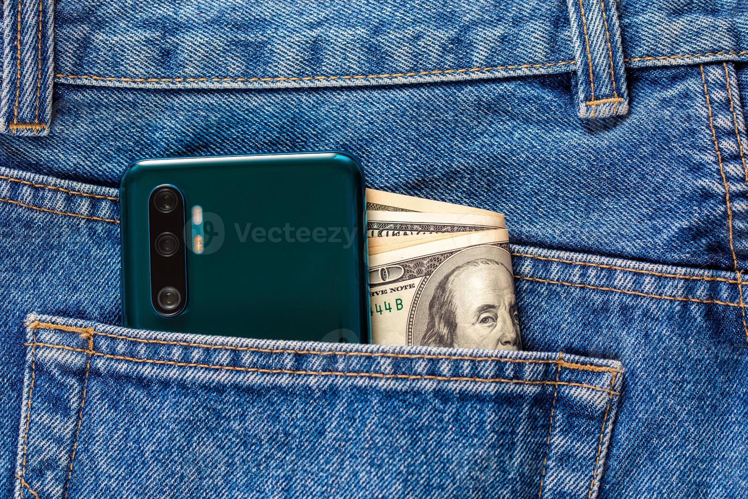 oss dollar sedlar och grön smartphone i de vänster bak- ficka av blå jeans. foto