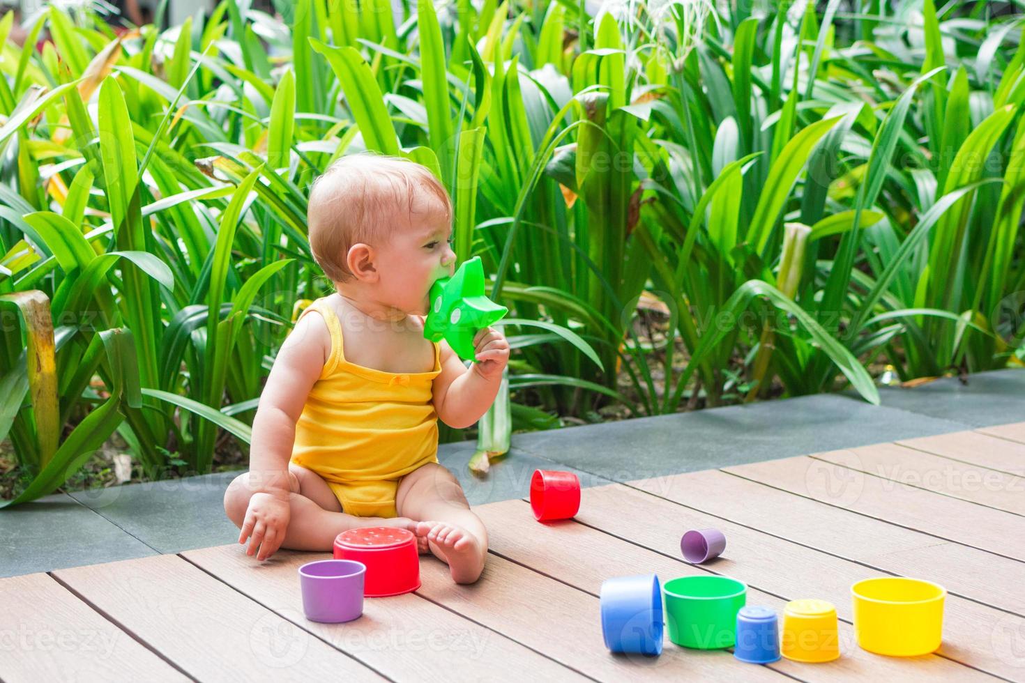 leende liten flicka spelar utomhus med färgrik plast konstruktör på en bakgrund av grön växter. foto