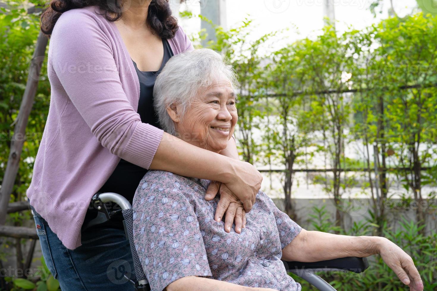 vårdgivare dotter hjälpa asiatisk senior eller äldre gammal dam kvinna på elektrisk rullstol i parken. foto