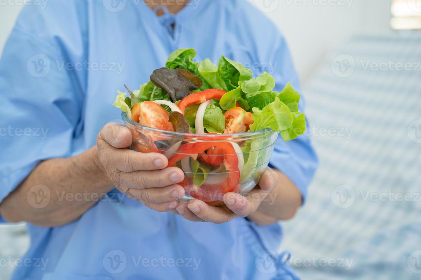 asiatisk senior eller äldre gammal damkvinna som äter frukost vegetabilisk hälsosam mat med hopp och lycklig medan du sitter och är hungrig på sängen på sjukhus. foto