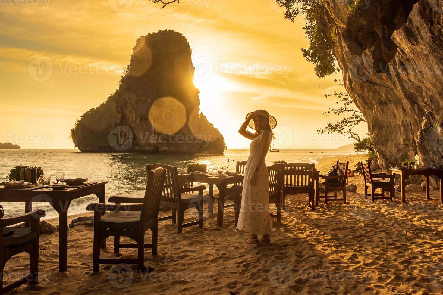 kvinna turist i vit klänning middag i restaurang grotta på phra nang stranden i solnedgången, railay, krabi, thailand. semester, resor, sommar, wanderlust och semester koncept foto