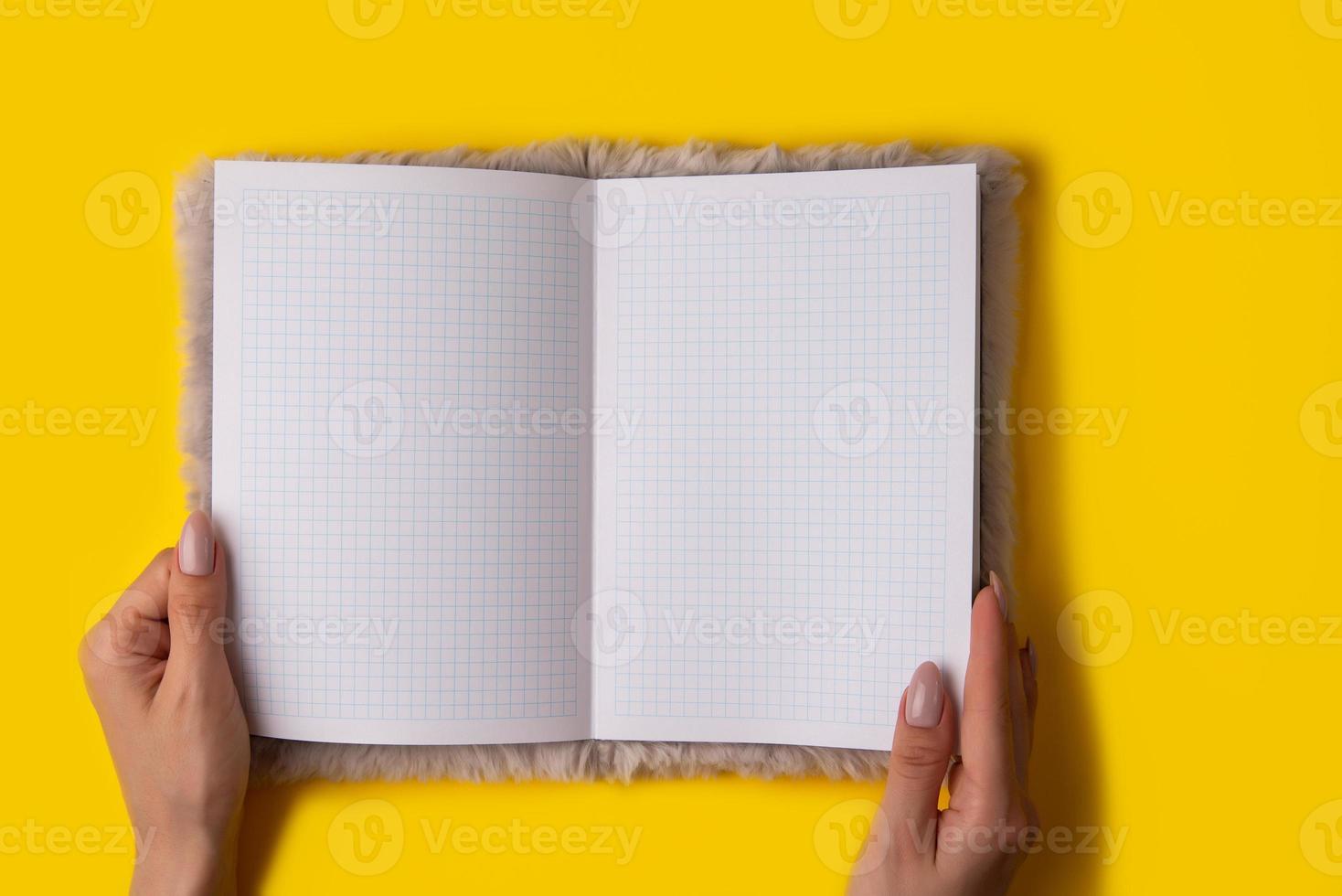 hand håll anteckningsbok tömma spridning på gul bakgrund. foto