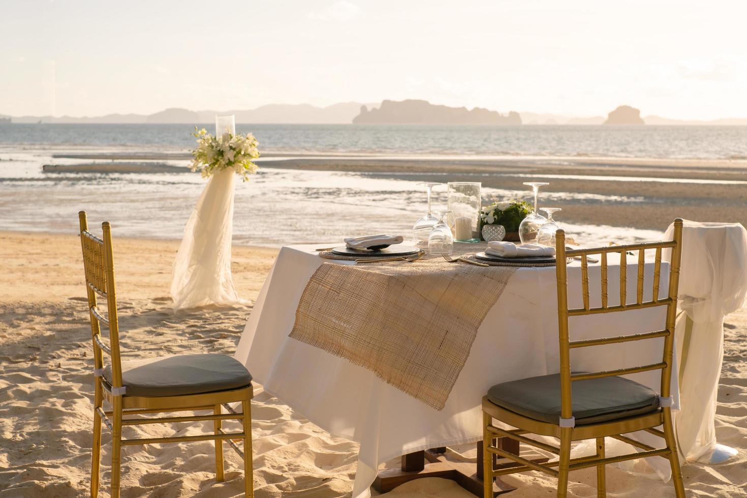 skön tabell uppsättning upp för en romantisk middag på de strand med blommor och ljus. catering för en romantisk datum, bröllop eller smekmånad bakgrund. solnedgång strand middag. vald fokus. foto
