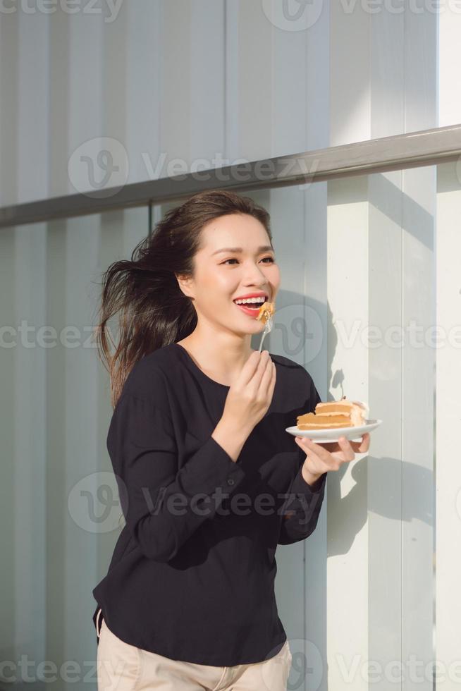 ung Lycklig kvinna står på de terrass av de hotell med maträtt kaka i de morgon. Söt asiatisk flicka i Bra humör och är redo för äventyr. foto